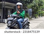 Small photo of Asian man work as a commercial motorcyle taxi driver taking order and looking for customer address from his smartphone