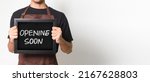 Small photo of Cropped portrait of Asian barista man holding a blackboard holding a blackboard that says "Opening Soon" good for banner. Isolated image on white background.
