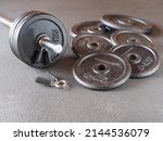 Small photo of Barbell and metal barbell discs, barbell plates with kilograms on the gray floor, copy space. Simulator for exercising and strengthening muscles. The concept of fitness, sports and weightlifting