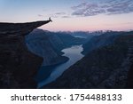 A woman sitting on the edge of Trolltunga in a beautiful morning sunrise in summer season, Odda town, Norway, Scandinavia, Europe