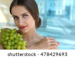 Woman holds grapes in the chest and hugs it with both hands. Beauty portrait with bare shoulders and her hair gathered against the glass background
