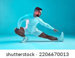 Stretching workout. Athletic flexible young man fitness trainer stretches leg muscles on blue background. Long exposure