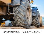 Small photo of Big rubber wheels of soil grade tractor car earthmoving at road construction side. Close-up of a dirty loader wheel with a large tread against the sky