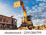 Small photo of A wheeled excavator loads a dump truck with soil and sand. An excavator with a high-raised bucket against a cloudy sky View from the trench. Removal of soil from a construction site or quarry