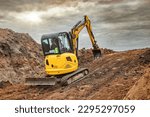 Mini excavator at the construction site on the edge of a pit against a cloudy blue sky. Compact construction equipment for earthworks. An indispensable assistant for earthworks