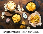 Small photo of Unhealthy food or snacks. All classic potato snacks with peanuts, popcorn and onion rings and salted pretzels in bowl plates on old wooden background. Unhealthy food for figure, heart, skin, teeth.