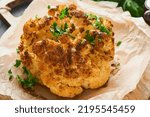 Small photo of Baked cauliflower. Oven or whole baked cauliflower spices and herbs server on wooden rustic board on old wooden vintage table background. Delicious cauliflower. Eyal Shani dish. Perfect tasty snack.
