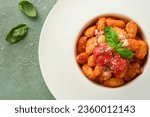 Potato gnocchi. Traditional homemade potato gnocchi with tomato sauce, basil and parmesan cheese on kitchen table on light green kitchen table background. Traditional Italian food. Top view.