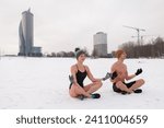 Young couple sitting in yoga at lotus pose after winter sauna. Cold exposure for better health and mood. Swim in ice cold water. Practice to boost immunity. Nordic lifestyle with the urban background