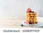 Stack of waffles with blueberries and strawberries on grey background, copy space