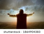 Rear view of Jesus Christ raised hands and praying to god with a sunrise sky background