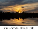 Small photo of Infernal sunset behind trees and reflection in water.