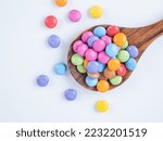 Bright multi coloured sugar coated chocolate candy presented on a teak spoon white background