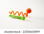 Small photo of googly eyed pom pom pipe cleaner orange wriggly worm green caterpillar funny character childs toy hand made isolated on a white background
