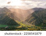 picturesque canyon between two mountain tops with green slopes , illuminated with golden sunset or sunrise rays and nice town below