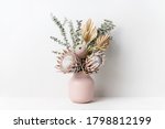Small photo of Beautiful dried flower arrangement in a stylish pink vase. In the flower bunch is pink King Proteas, Banksia, Eucalyptus leaves and golden Palm frond photographed on a white background.