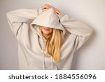 Young beautiful girl in a white hoodie posing. Warm oversized hoodie with an hood. Stylish trendy hipster bow. Trying on clothes in a store. Youth subculture. Fashion clothing advertising