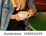 Woman with a cup of aromatic coffee in her hands sits on the summer terrace of the restaurant. The girl drinks coffee after breakfast. Delicious hot latte in a white cup. Quiet freelance lifestyle