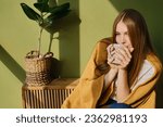A cup of tea or coffee in the hands of a girl. In the morning the girl drinks hot tea. Enjoy the comfort of home. Close-up of a cup in the hands of a woman in the sun. Warmth and comfort