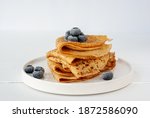 Vegan crepes made from chickpea flour, al purpose gluten free flour and oat milk, with frozen blueberries on a white wooden table