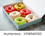 Six assorted glazed sweet donuts in a paper box on a table