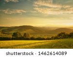 Sunset over hilly landscape, the golden glow of the setting sun, meadow in the foreground