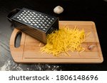 grated fresh aromatic cheese for pizza, garlic and grater lie on a wooden kitchen board