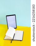 Small photo of Blank tablet and ope notebook with pencil on yellow and blue background, work desk with copy space, writer's workplace, online studying