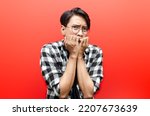 Small photo of Asian man is terrified covering mouth and trembling isolated on red background. asian man scared and making frightened gesture. horror concept.