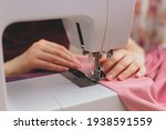 Happy attractive young woman seamstress sitting and sews on sewing machine in studio