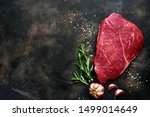 Raw beef steak with spices on a dark slate, stone or concrete background. Top view with copy space.