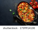 Stuffed pasta cannelloni with minced meat baked in  tomato sauce in a skillet on a dark slate, stone or concrete background. Top view with copy space.