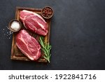 Raw organic marbled beef steaks with spices  on a wooden cutting board on a  black slate, stone or concrete background. Top view with copy space.