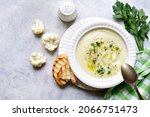 Small photo of Cauliflower creamy soup with potatoes and cheese in a white bowl over light slate, stone or concrete background. Top view with copy space.