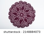 A dark red crochet doily on a white background