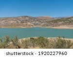 Beninar reservoir between mountains in southern Spain, there is vegetation of shrubs and trees, the sky is clear