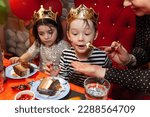 Small photo of Moscow, Russia - 03 - 26 - 23: A boy and a girl wearing golden crowns eating birthdya cake, mom helping. Spoiled children concept, bday party, festival, queen, king, costumes.