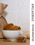 Small photo of Vertical pastry background. Close-up of a white dish with laid sesame cookies. Nearby are cookies in a kissable wrapper, behind a paper bag and a rolling pin.