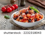 Pasta Alla Norma. Delicious Sicilian pasta dish with roasted eggplant, marinara tomato sauce, grated ricotta and fresh basil served in a white ceramic bowl. Wooden table, selective focus, horizontal.