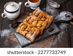 Homemade sweet puff pastries. Baked Puff pastry turnovers with chocolate and fruit filling served on a wooden board with cup and teapot on background. Selective focus, horizontal.