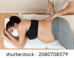A pregnant woman wearing face mask lying on her side on a massage table while a physiotherapist massages