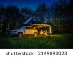 Man and women with dogs camping in front of a 4x4 Offroad vehicle with roof tent at night time and romantic lighting