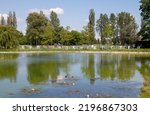 Small photo of KRAKOW, POLAND - JUNE 1, 2022: Polish Airmen Park (Park Lotnikow Polskich) with pond and paved paths. Recreational area in Krakow. Ogrod Doswiadczen, Stanislaw Lem's gardens full of experiments in bg.