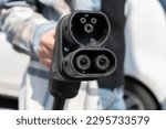 Small photo of Woman holding CCS fast charging socket type 2. Combined Charging System Combo 2 connector plug for electric vehicles at EV car charging station. Female hand plugging in charger into electric car.