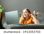 Happy relax young woman lies on sofa with laptop in headphones. Remote work, online study, online shopping watching films or video call on laptop. Teen girl rest at home interior of living room
