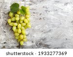 Large ripe green Riesling grape grone. Ripe juicy grapes with vine foliage on light gray concrete background with copy space top view.