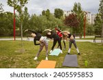 Small photo of Fellow athletes doing stretching exercises with skilled trainer in green park. Professional fitness coach leads fellows on workout class