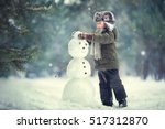 Cute little boy in earflaps hat is making a snowman. Image with selective focus and toning