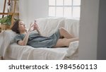 happy asian woman face relaxing using mobile smart phone surfing internet and chat on sofa couch at home. female laying down in living room embarrassed smile when using mobile phone. woman laugh happy
