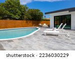 Small photo of Backyard of elegant house in the Highland Lakes neighborhood of Miami, short grass, white walls, mirrored windows, swimming pool, sidewalk, wooden fence, black tiles, blue sky, palms, sun loungers
